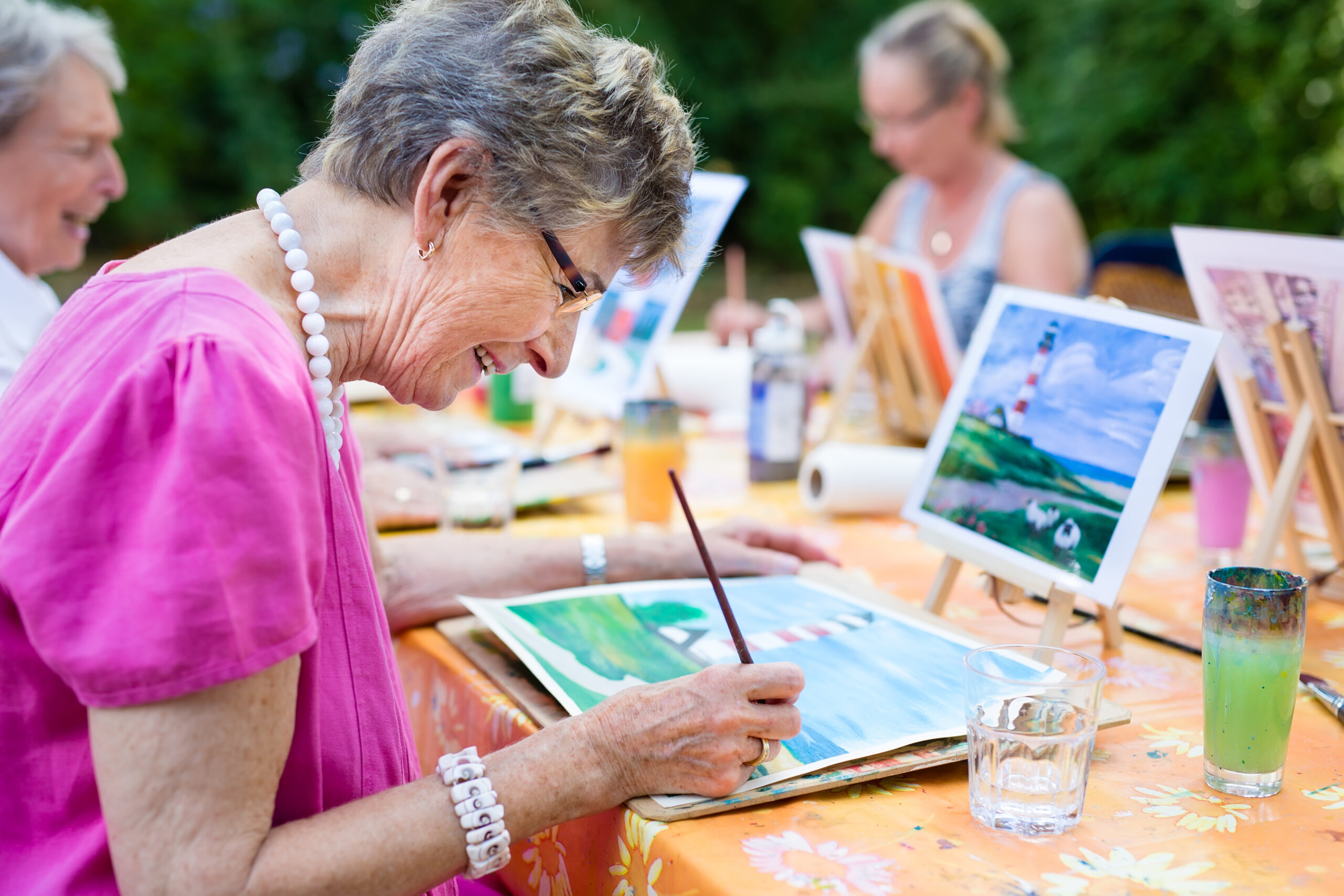 Side view of a happy senior woman smiling while painting as a recreational activity or therapy outdoors together with the group for her high school reunion