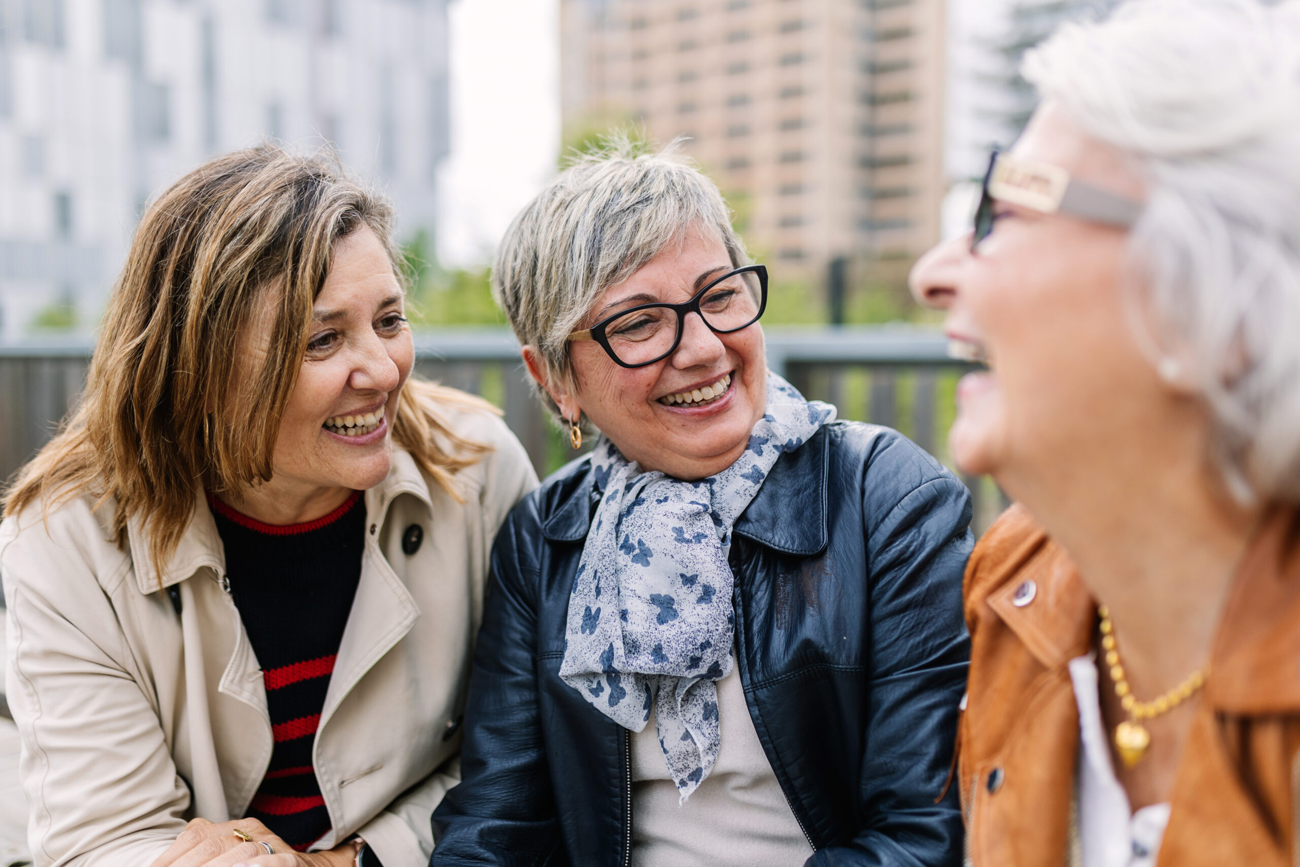 Three mature retired women laughing while talking sitting outside. Small group of mature females having fun enjoying a conversation bonding at city street. Elderly friendship concept. high school reunion together