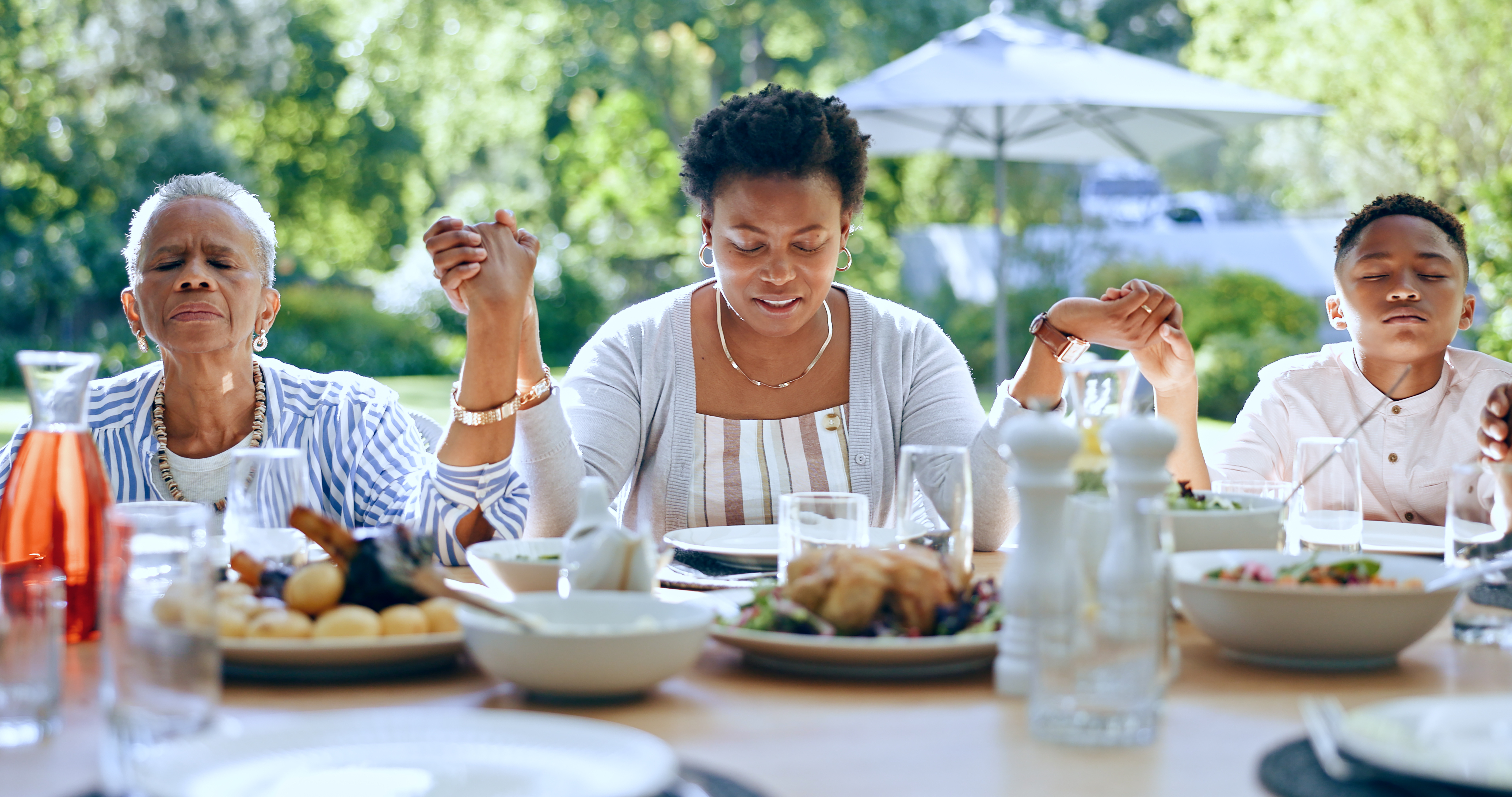 family prayer, Holding hands, black family or kid praying for food to worship God together for faith or gratitude. Grandmother, backyard or African mom with child in nature for a meal, brunch or lunch with grace