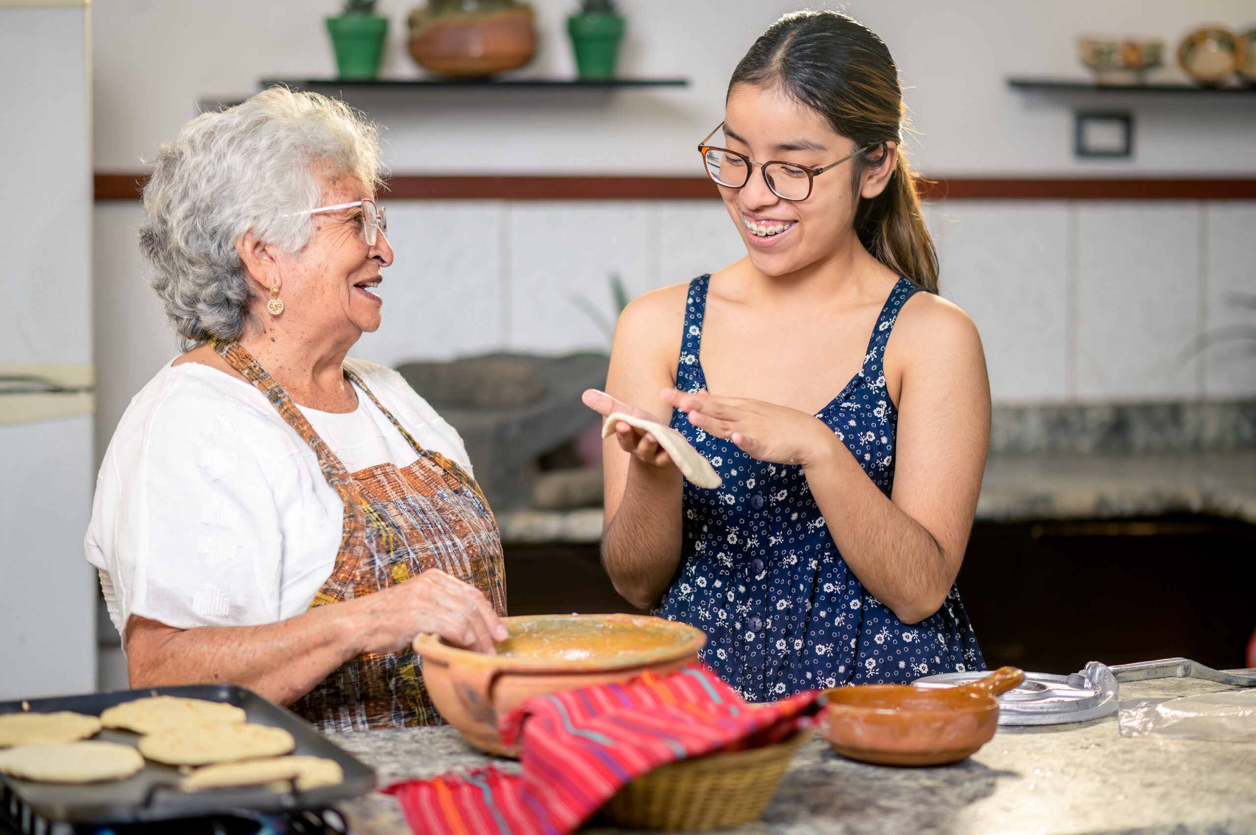 Grandmother and granddaughter make corn tortillas at home.